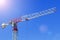 Ndustrial construction crane or column-jib crane with cabin works on the construction site and blue sky with rays fron