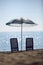 Near sea ashore two chairs stay under umbrella