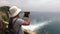 Near the wooden fence is a tourist girl and takes pictures of a beautiful waterfall and the blue sea