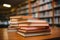 Neat stack of books on table, library bookshelf blurred behind