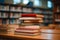 Neat stack of books on table, library bookshelf blurred behind