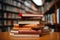 Neat stack of books on table, library bookshelf blurred behind