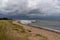 Neat waves breaking on a sandy beach with marsh grass and sand dunes and a dark ominous sky overhead