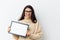 neat woman in a beige turtleneck sweater and black-rimmed glasses, standing on a light background holding a white frame