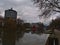 Neckar river in center with railing, promenade, trees and office building Neckarturm on cloudy day in winter.