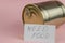 Need food. Business card with handwritten text and canned food against a pink background. Gold-colored tin. Concept of helping the