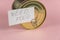 Need food. Business card with handwritten text and canned food against a pink background. Gold-colored tin. Concept of helping the