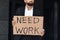 Need work. Unrecognizable male office worker holding cardboard sign, standing outdoors near business center, crop