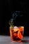 Negroni cocktail with smoking rosemary and orange garnish on black background