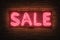 Neon sale sign on brick wall, vibrant urban advertising