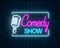 Neon sign of comedy show with retro microphone symbol on a brick wall background. Humor glowing signboard.