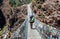 Nepal Porter carrying heavy load on his back going along the bridge