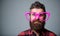 Nerd concept. Hipster looking through of giant pink eyeglasses. Man beard and mustache face wear funny big eyeglasses