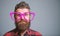 Nerd concept. Hipster looking through of giant pink eyeglasses. Man beard and mustache face wear funny big eyeglasses