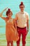Nerds` honeymoon concept. Portrait of couple of young happy married hipsters in trendy clothes standing together on the beach wit
