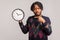 Nervous african man with beard and dreadlocks pointing finger on clock in his hand with serious face, time management, schedule