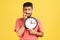 Nervous anxious bearded man instripe t-shirt biting nails on his fingers holding big wall clock in hand, worried about deadline