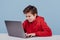 Nervous child boy in red sweatshirt typing on laptop