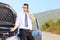 Nervous man standing next to his broken car and talking on a phone