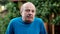 Nervous stressed mature man feeling awkward looking with doubt at camera standing on formal garden background.