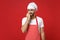 Nervous young bearded male chef cook or baker man in striped apron white t-shirt toque chefs hat posing isolated on red