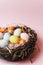 A nest of twigs and hay and a pink paper filler with pastel colored Easter eggs. Painted and decorative eggs for a light Easter