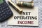 NET OPERATING INCOME - words on white paper against the background of a table of numbers with a calculator and banknotes