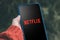 Netflix logo on a smartphone, global provider of streaming movies and TV series. Woman watching video by Netflix service on