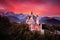 Neuschwanstein fairy tale castle. Beautiful sunset view of the bloody clouds with autumn colours in trees, twilight night, Bavaria