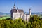 Neuscwanstein castle on the mountain with green fields and blue sky on the background