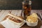Neutral view of a hotdog with chimichurri sauce with soda and potato chips on a rustic table. Fast and junk food concept