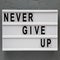 `Never give up` words on lightbox over gray background. Flat lay, from above, overhead. Close-up