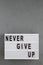 `Never give up` words on lightbox over gray background. Flat lay, from above, overhead. Copy space