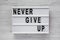 `Never give up` words on lightbox over white wooden background. Flat lay, from above, overhead. Close-up