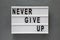 `Never give up` words on modern board over concrete background. Flat lay, from above, overhead. Closeup