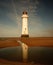 New Brighton Lighthouse reflecting on the water surrounded by sand under a blue sky