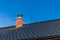 New chimney pipe in red bricks on roof in black shingles. On blue sky. Construction of a family house. Detail of the roof