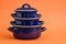 New And Clean Covered Dark Blue Saucepans on Orange Background