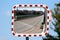 New convex rectangular traffic mirror with red and white striped frame mounted on strong metal pole with old green bridge