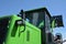 New green bulldozer cabin with exhaust pipe stake, diesel motor compartment, headlights and loader bucket against blue sky