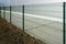 A new green metal wire fence around a new gray industrial facility, soil for grass and a paved lane