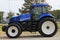 A New Holland farm tractor parked in a parking lot with green grass that`s bright and colorful.