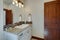 New luxury bathrooms with rich color wooden doors, natural beige countertops, white cabinets and sinks. Bright clean grey walls