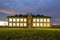 New modern two-storied kindergarten preschool building with brightly lit windows on green grassy lawn and evening blue sky copy