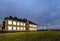 New modern two-storied kindergarten preschool building with brightly lit windows on green grassy lawn and evening blue sky copy