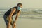 New normal beach jogging workout - young fit and attractive man in face mask breathing tired doing cool off after running on sea