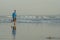 New normal beach running workout - wide lens view of young fit and attractive man jogging barefoot on sea wearing face mask