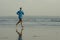 New normal beach running workout - wide lens view of young fit and attractive man jogging barefoot on sea wearing face mask