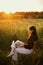 New office concept. Fashionable elegant girl working on laptop and sitting on rustic chair  in sunny summer field at sunset.