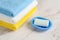 New rectangular soap bar on a blue dish near a stack of colored cotton terry towels over marble surface. Washing hands with soap.